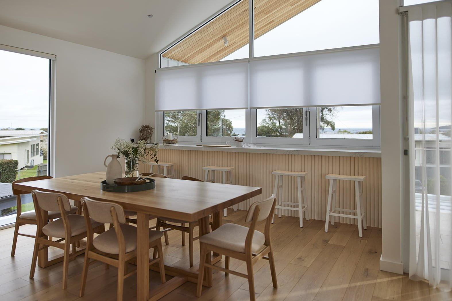 A dining space with motorised roller shades at the window