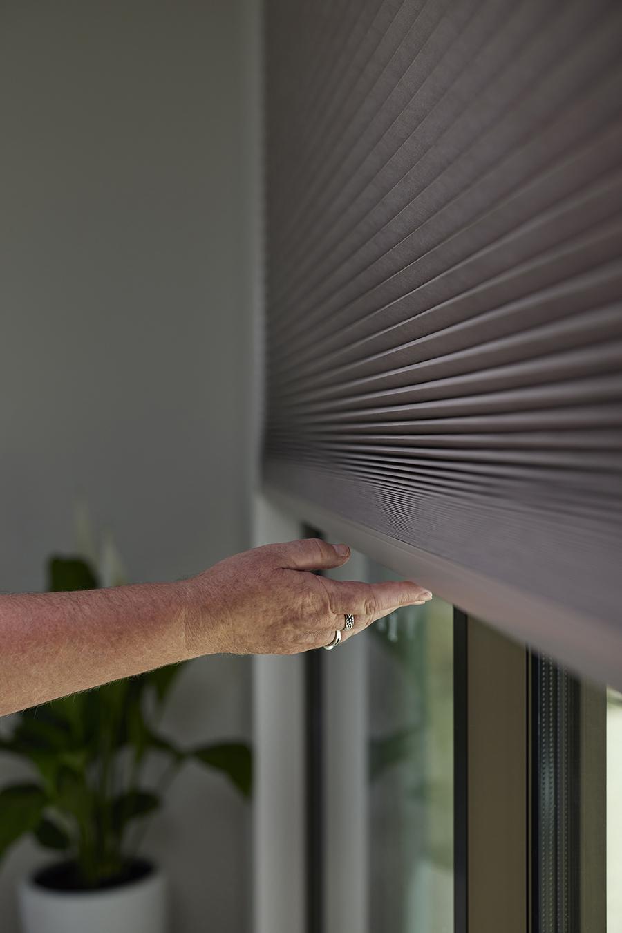 A hand touching the bottom rail of a honeycomb shade
