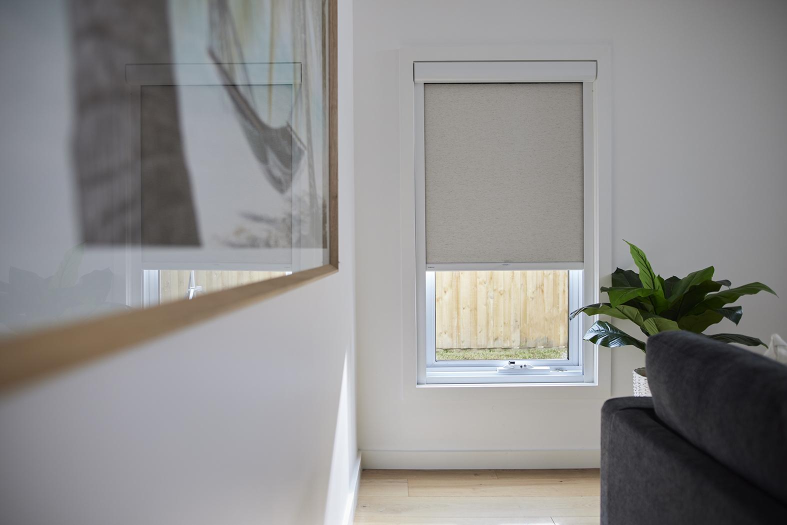 A light grey roller shade in a white encased headrail with side tracks, lowered part way over a living room window