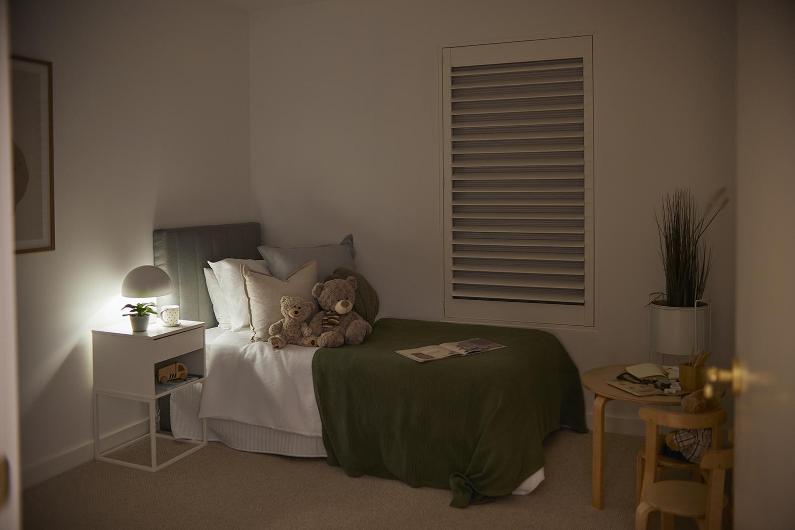 A childs bedroom with a blockout shutter at the window, with the louvres open and the honeycomb shade pulled down behind it. 