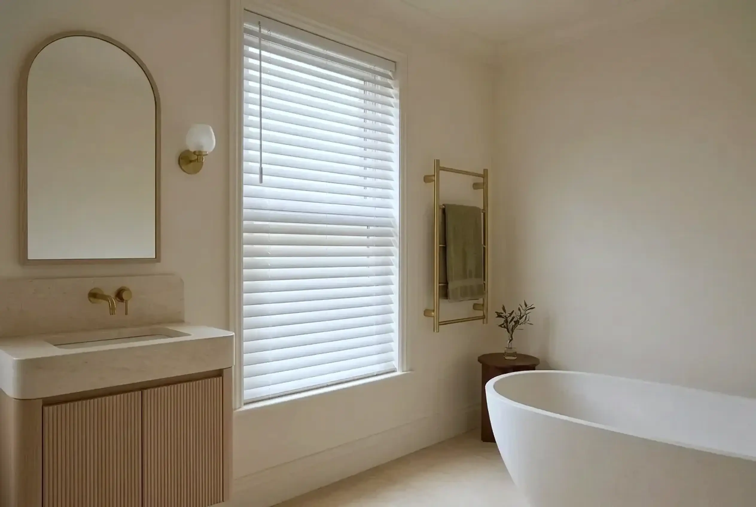 White faux wood venetian blind in a serene bathroom with a freestanding stone bath, brass towel rail and fluted limed-oak vanity with a limestone basin.